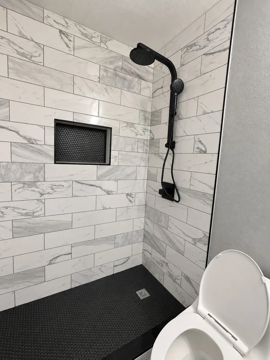 Black and white walk-in shower with marble-look tile and black fixtures