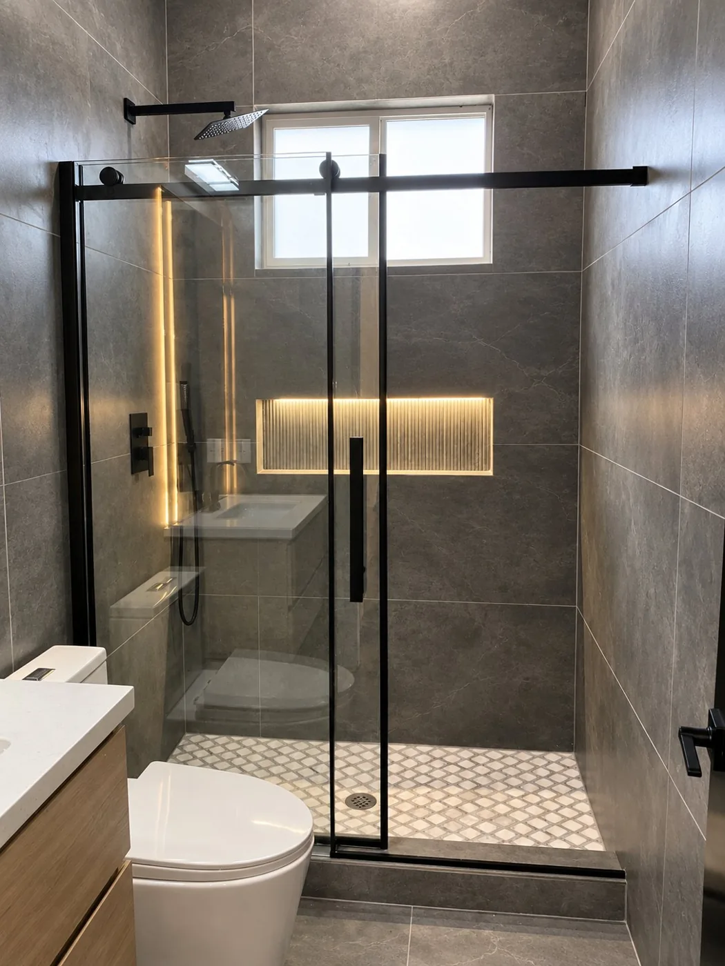 Modern gray tile shower with black framed glass enclosure and illuminated niche